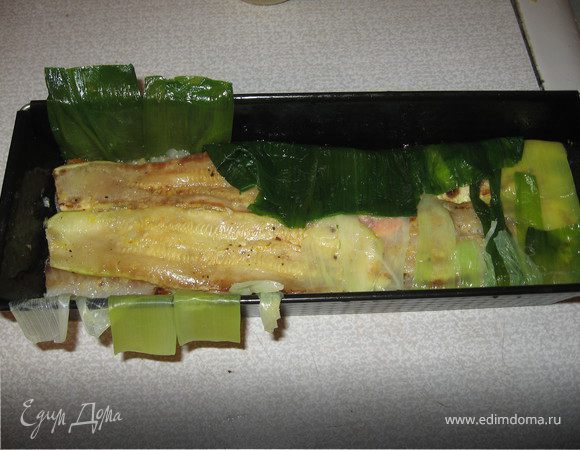 Нарезать оба вида рыбы тонкими ломтиками - 1,5-2 см. Выложить слоями в форму продукты: красная рыба, перцы, цукини, белая рыба, перцы, цукини - каждый слой промазывая чесночно-лимонной заправкой и слегка прижимая слои руками через пленку.
Когда продукты закончатся полить верхний стой остатками заправки, накрыть свисающими листьями порея внахлест. Закрыть форму фольгой и запекать при 160 градусах около 40 минут. 
Затем остудить, поместить на фольгу по всей длине формы небольшой груз и отправить в хол-ник на 4 часа. 
Подавать холодным, нарезав очень острым ножом толстыми ломтиками.