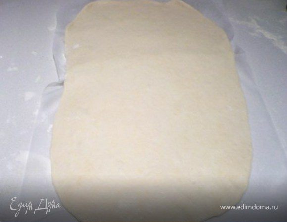 Посыпать стол мукой и, раскатать тесто в форме прямоугольника, побив его сначала  скалкой.  Я раскатываю на кальке, посыпанной мукой, так как  потом  будет  легче «вертеть» тесто чтобы удобнее  было раскатывать.  
