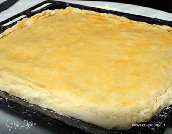 Раскатать вторую половину теста и накрыть начинку, закрепив края, чтобы начинка не вытекла.
Кисточкой смазать тесто оставшимися желтками