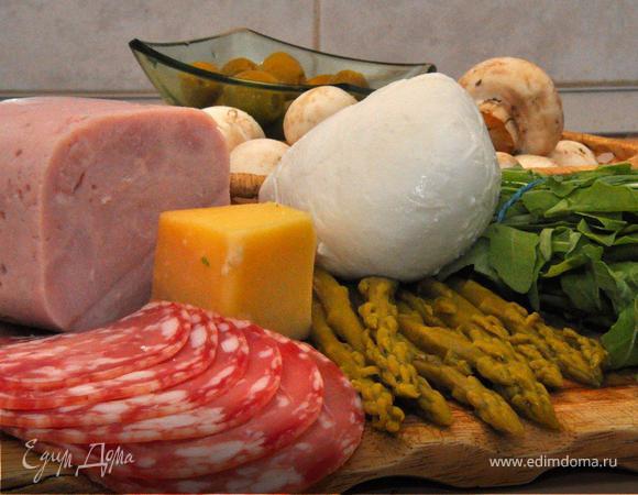 Тесто раскатать толщиной 5мм и диаметром 30см. Выровнять края, используя плоскую тарелку такого диаметра. Положить тесто на кулинарную бумагу, полить готовым соусом и равномерно выложить начинку.  Плоские кусочки ветчины, салями, тонко порезанные грибы, половинки оливок, кусочки артишоков или спаржи, моцареллу тоже кусочками. 