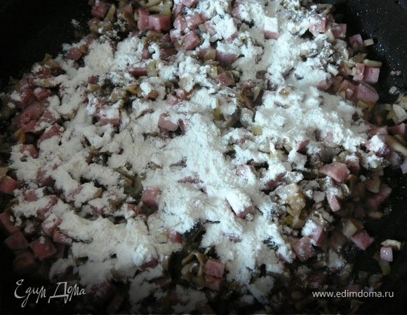 Шампиньоны,ветчину нарезать и добавить к луку. Приправить перцем и сухим базиликом.Обжарить пару минут и добавить муку. 