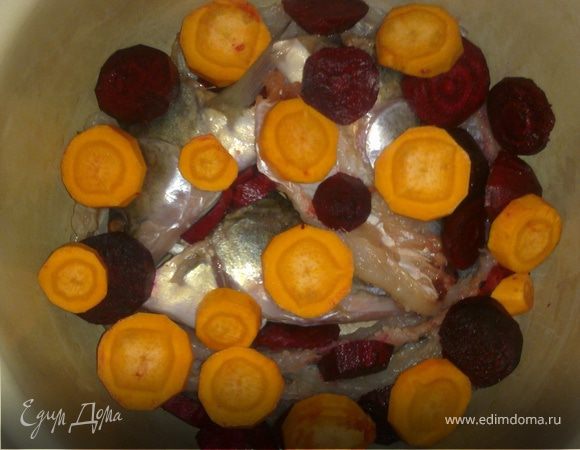 В глубокую кастрюлю на дно выложитьголовы, хребты, хвосты и крупные плавники. Морковь и свеклу почистить, нарезать кружочками и выложить на косточки. 