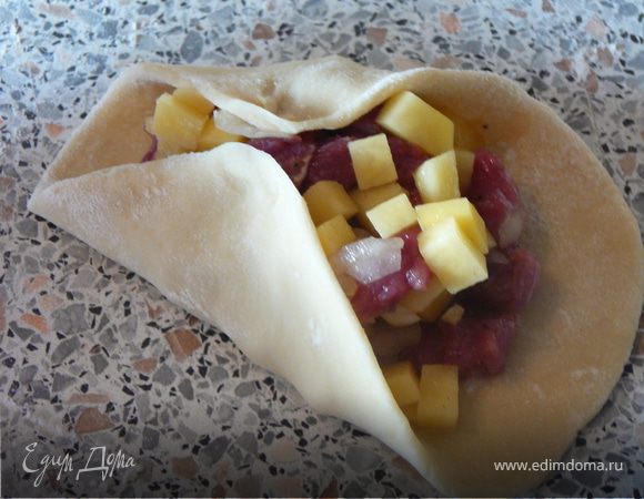 Теперь самый сложный момент — формирование из кружка треугольника. Пальцами аккуратно поднимите противоположные края теста и защипните сначала одну сторону.