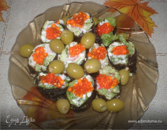 Прессованные листья морской капусты разложить на столе,слегка сбрызнуть водой,сверху положить листья салата, смазать их мягким плавленным сыром, сверху слоем выложить натёртый на крупной терке свежий огурец смешанный с мелко рубленной зеленью,затем уложить сёмгу кусочками или крабовые палочки в линию. Закатать рулетом. Дать пропитаться 20 мин, порезать на равные кусочки. На блюдо уложить листья салата, разложить ролы и украсить оливками.Можно украсить ролы красной икрой.