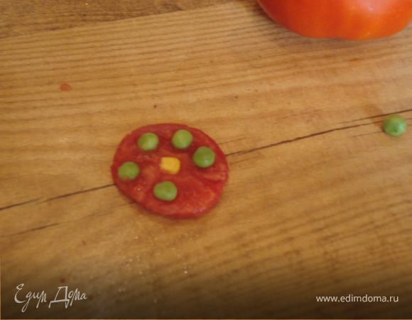 Берем половину большого и маленького помидора.От половинки маленького помидора отрезаем сверху тонкий ломтик. На отрезанный ломтик приклеиваем капелькой майонеза половинки горошин и зернышко кукурузы. Этот ломтик будет служить "диском набора".