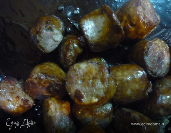 В выделившимся жиру немного обжариваем нарезанную кусочками по 4-5 см колбаску. Колбаску тоже отправляем в горшочки по 4 кусочка на порцию.