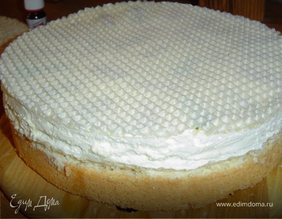 Теперь собираем торт. Первый бисквитный корж смазываем кремом, на него выкладываем вафельные коржи с суфле.Сверху накрываем вторым бисквитным коржом и смазываем его и бока кремом.