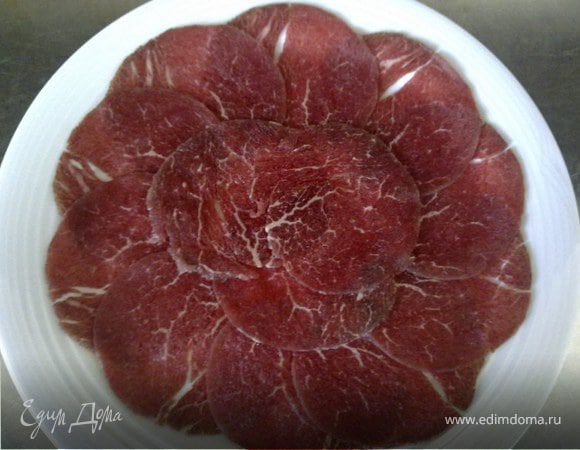 Нарезать мясо на слайсере толщиной 0,5 мм и выложить на большую тарелку. Посыпать солью с перцем и полить апельсиновым соком.