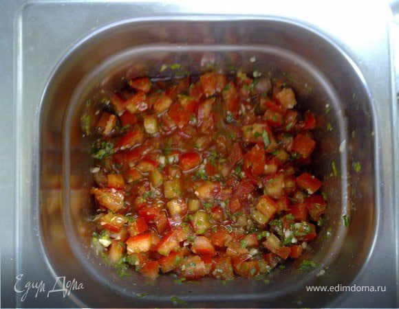 Помидоры очистить от кожицы и удалить сердцевину (сок и семена). Мякоть нарезать на мелкие кубики. Все выложить в миску, посыпать солью, перцем и орегано. 

Добавить мелко нарубленный чеснок, заранее замаринованный в оливковом масле, петрушку и базилик. Заправить маслом.
