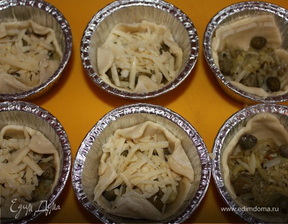 Разогреть духовку до 200 градусов. Картофель почистить и натереть на крупной терке, смешать с солью, рубленым чесноком, перцем и прованскими травами. Обжарить на растительном масле постоянно помешивая, до золотистого цвета. Сыр натереть на терке. Тесто разрезать на квадратики приблизительно 10х10см. В формочки для кексов положить квадратики теста. Начинить картофелем, тремя каперсами и тертым сыром. Уголочки теста загнуть.