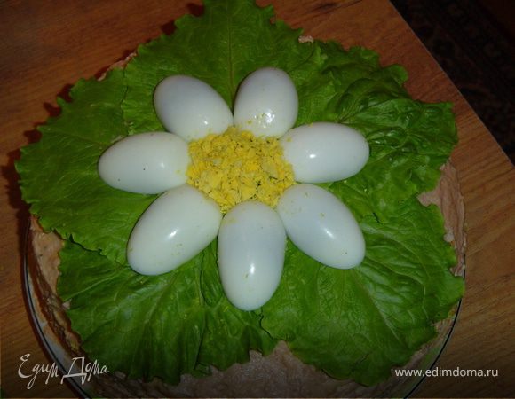 А теперь украшаем готовый торт.На торт кладем листья салата, отварные яйца разрезаем вдоль на две части, удаляем желток, а белки выкладываем виде цветка. Желток растираем и выкладываем в центр «цветка». 