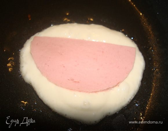 Выкладываем на сковороду с раскаленным растительным маслом половину ложки теста, сверху ложим ломтик колбасы и придавливаем пальчиками.