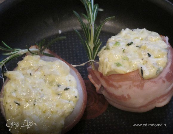 Я, как правило, заворачиваю луковицы в добрый ломтик копченой грудинки или бекона и закрепляю при помощи заостренной веточки розмарина или простой палочки для коктейля. Розмарин и грудинка высвободят головокружительные ароматы во время запекания. Поместите луковицы на противень и залейте получившуюся луковую смесь в каждую из них. Поставьте в духовку на 25 минут. Им предстоит сделаться мягкими и нежными. Можно также экспериментировать с различными сырами.