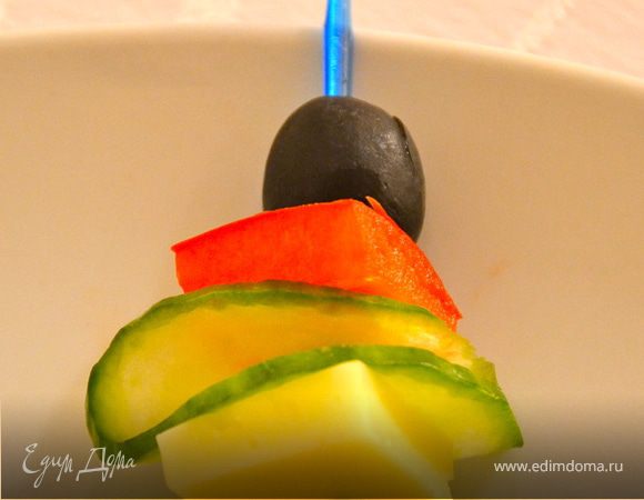 Нанизать на шпажку целую маслину, квадратик красного перца, кружочек свежего огурца, сложенного пополам и квадратик сыра