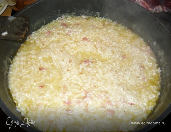 Мелко нарезать лук, чеснок и бекон. Слегка обжарить их на оливковом масле так, чтобы они стали мягкими, но ни в коем случае не зажаривались. Добавить рис, прогреть пару минут, дав ему пропитаться маслом. Влить вино и дождаться пока оно выпарится.
По половнику добавлять бульон, не допуская, чтобы рис в нем плавал. Он должен потихоньку впитывать в себя жидкость. Посолить. 