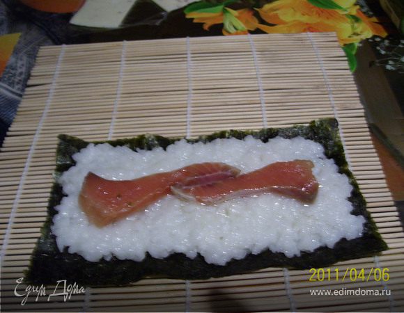 Разрезаем лист нори пополам вдоль. Укладываем на циновке блестящей стороной вниз. Берем рис и равномерно распределяем по листу, оставляя по краям нори 0.5 см. Середину рисового листа смазываем васаби. Вдоль слоя васаби укладываем рыбу.