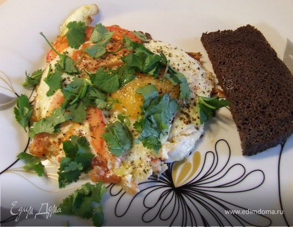 Разогреть сковороду, влить масло, обжарить мелконарезанный лук, разбить яйца, посолить. Нарезать помидоры и выложить сверху яиц.Жарить до готовности. Добавить специи и зелень. Приятного аппетита!