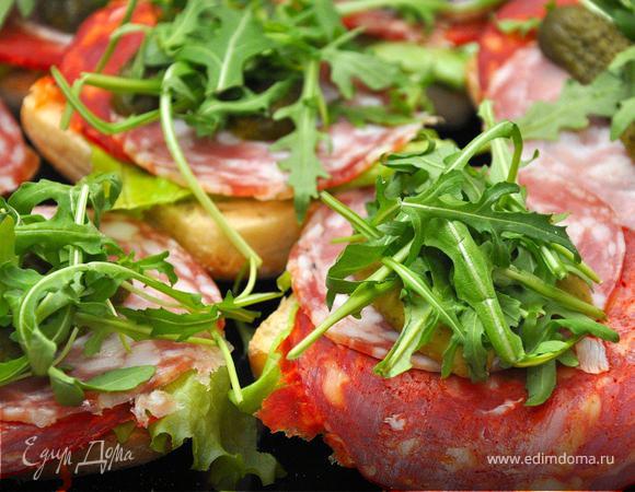 1.Chorizo & Salchichon Bruschetta
Начнем с простейшего и вместе с тем очень вкусного. Сделаем брускетты с испанскими сыровялеными колбасами. Они обладают потрясающим ароматом и вкусом и идеально подойдут на закуску нашим болельщикам. Для этого нарежем чиабатту, и отправим ее в тостер, немного поджарится, затем намажем наш хлеб плавленым сыром, потом положим лист латука, теперь по кусочку чоризо и сальчичона, сверху корнишоны и рукколу. Брускетты готовы.
