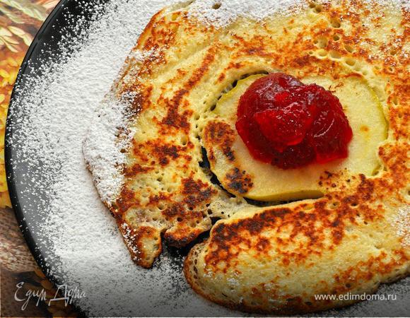 Теперь берем разогретую сковородку, добавляем немного растительного масла, кладем в центр кружок яблока и наливаем половником тесто вокруг него, чтобы оно растеклось и покрыло всю свободную поверхность. Поставим сковородку на средний огонь и жарим около 3 минут, пока поверхность блинчика не станет сухой, а краешки не зарумянятся.  Используя широкую лопатку, перевернем блин и жарим еще полминуты. Выкладываем блинчик на широкую тарелку, поверх поджаренного яблока выложим ложку фруктового джема, а края блинчика и тарелки обсыпим ванильной сахарной пудрой. Прекрасный десерт к «масленичному» столу!