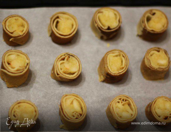 Яблоки почистить, удалить сердцевину, нарезать кубиками. На сковороде на среднем огне тушить яблоки 10 минут (воду и масло добавлять не надо). Добавить сахар и корицу, тушить еще около 10-15 минут.
Остудить. На блинчик выложить начинку.  
Свернуть рулетик. Нарезать кусочками шириной 1-1.5 см. Противень застелить бумагой для выпечки или смазать маслом.
Выложить рулетики.