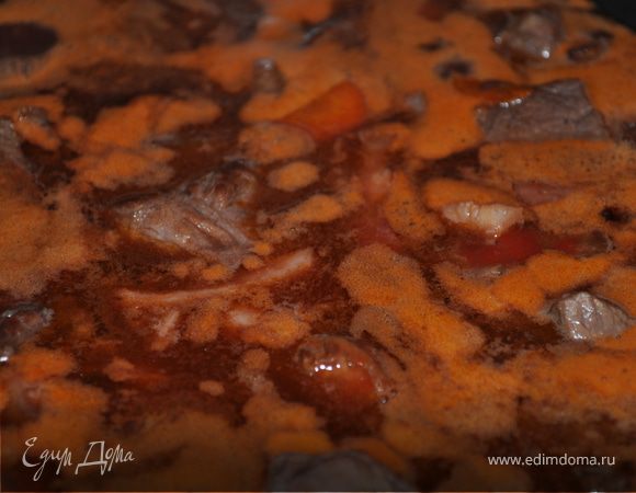 Убавьте температуру духовки до 160 градусов. 
Залейте в мясо вино, добавьте бульон, так чтобы он едва покрывал мясо. Добавьте томатную пасту, раздавленный чеснок, лавровый лист. Доведите до кипения на плите. Закройте крышкой и поставьте в духовку на 3-4 часа. Мясо в духовке должно слегка кипеть.