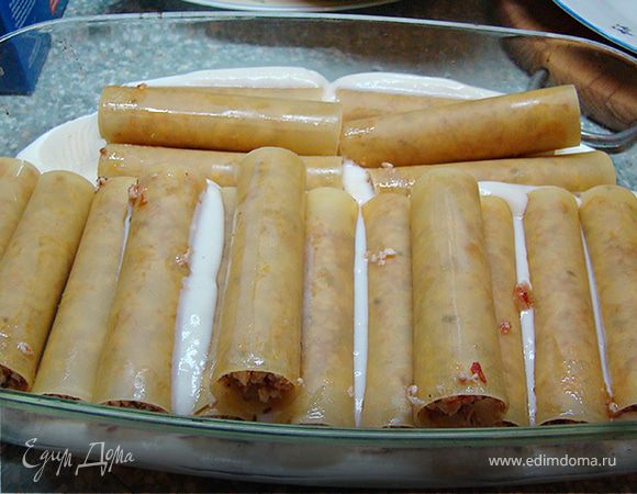 Форму для запекания наполните половиной соуса бешамель. Выложите туда заполненные фаршем каннелони.