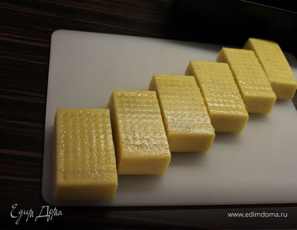 Нарезаем остывшую поленту на порционные кусочки и укладываем на противень.