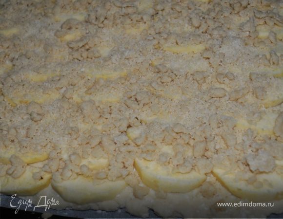 Противень застелить бумагой для выпечки и раскатать на нем тесто. 
Яблоки очистить от кожуры, нарезать дольками и выложить поверх теста плотными рядами наподобие черепицы. Посыпать крошкой. Для ее приготовления нужно смешать все составляющие в крошку, при необходимости добавить немного муки.