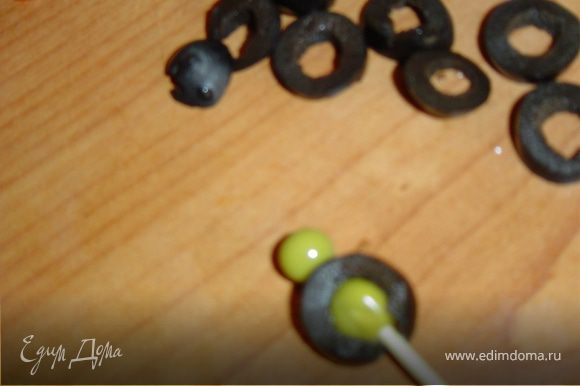 Нарежьте маслины поперек кружочками, кружочки нанизывайте на зубочистки, насадив горошины внутрь и сверху.