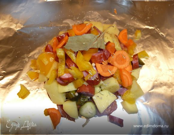 Собираем блюдо на 1 порцию: на лист фольги (примерно 30х30 см) в центр выкладываем слоями (немного солим и перчим каждый слой): мясо, чеснок (втыкаем в мясо), лук, корнишоны, сельдерей, картошку, колбаски, болгарский перец и морковь. В центр кладем часть лаврового листа, несколько горошин черного или белого перца, немного солим.
Можно сверху в центр влить 1 ст.л. красного сухого вина ИЛИ острой томатной пасты. 