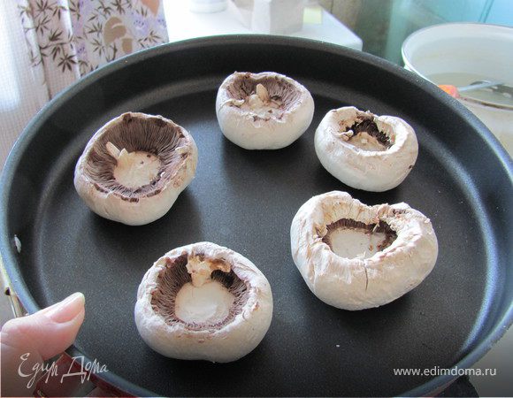 Для начала картошку нарезаем очень мелкими кубиками и их оставляем в воде до тех пор пока остальная часть начинки не будет готова. Это поможет нам избавиться от лишнего крахмала. Затем чистим грибы и вынимаем плодоножки, раскладываем их на форму для выпекания. Никакого масла не добавляем, грибы и начинка будут очень сочные и ничего не пригорит.