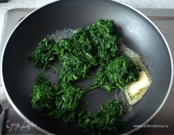 Тем временем размораживаем шпинат в кипящей воде, воду сливаем. На сковороде в оставшемся масле обжариваем шпинат на среднем огне в течение 3-х минут. 