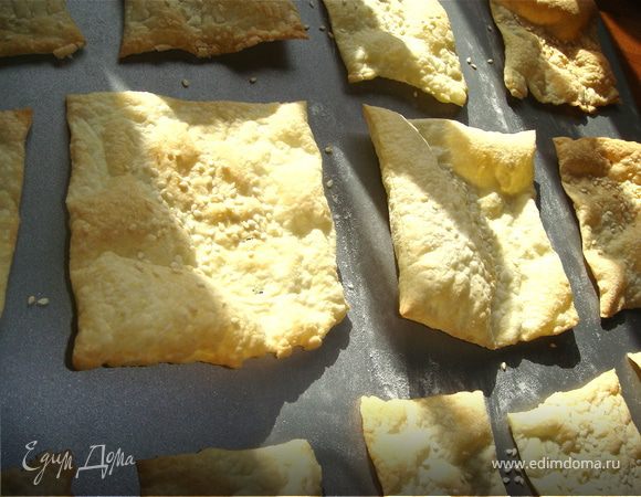 Слоеное тесто раскатать как можно тонко и нарезать на квадраты 10х10. Присыпать сверху кунжутным семенем и выпекать в духовке 220С до золотистости.
