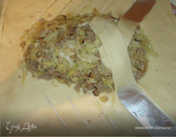 Начиная с углов, делаем надрезы до начинки шириной около 3-4 см, как указано на фото.
Складываем получившиеся полоски косичками внахлёст, оставляя только первые и последние.
Из верхней части складываем голову, а из нижней - хвост "крокодила".
Формируем ноздри у "крокодила", из обрезков теста лепим "лапки" и "глаза-брови".