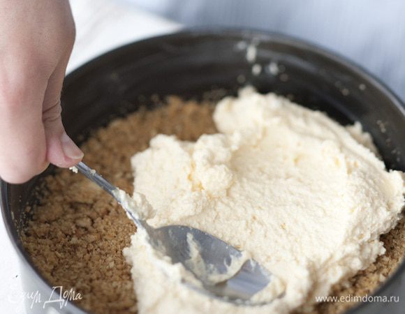 Смазать разъемную форму для выпечки оставшимся сливочным маслом. Выложить сначала массу из крошек, а сверху — творожную массу.