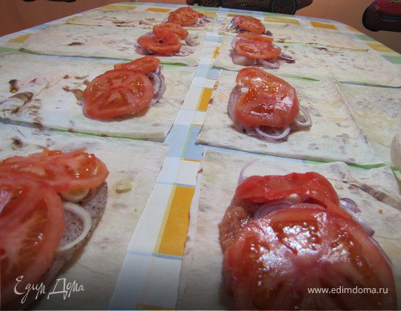 Выложить на лаваш по куску рыбного филе, посыпать колечками лука, добавить 2 кружочка томата.