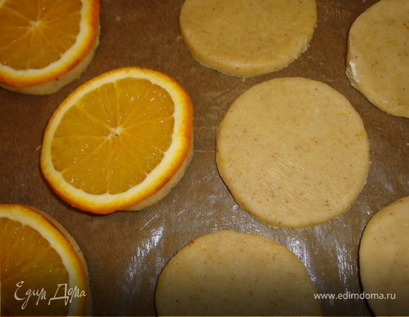 По истечении времени достать тесто и раскатать его. Для этого я положила тесто на чуть присыпанное мукой силиконовое полотно и, обернув скалку пленкой, раскатала. Стаканом вырезала кружочки. Лопаткой с острым краем переложила кружочки на чуть смазанную маслом бумагу для выпечки, которая, естественно, уже лежала на противне.
Апельсин помыла-обсушила и нарезала кружочками, довольно тонкими (ок. 3 мм.). На каждый кружочек теста положила по кружочку апельсина.