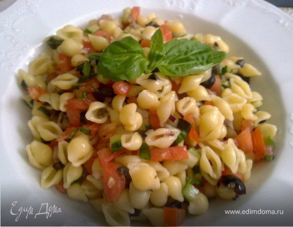 Отварить до al dente ракушки и 2 зубчика чеснока. Слить и промыть холодной водой чтобы ракушки остыли. Чеснок отложить в сторону- он пригодиться для заправки.
Порезать помидоры, оливки, шнитт-лук, базилик, огурец на кусочки, примерно в 2 раза меньше, чем одна ракушка и все смешат с ракушками.
1 зубчик свежего и 2 зубчика варёного чеснока растолочь в ступке, добавить к чесноку уксус, масло, соль, перец.  Полить салат заправкой.
