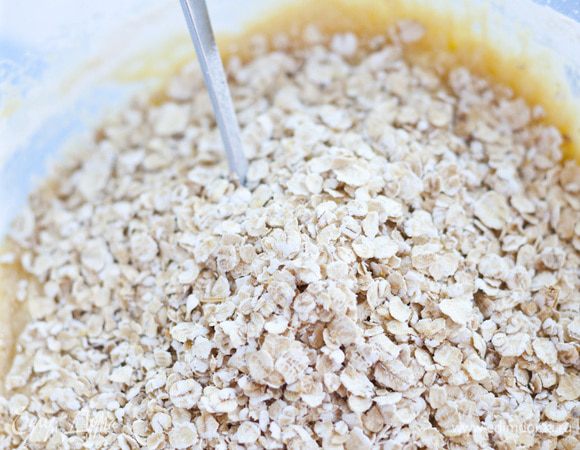 Влить 1/2 стакана теплой воды, ванильный экстракт, затем добавить муку, овсяные хлопья и изюм. Все еще раз перемешать.