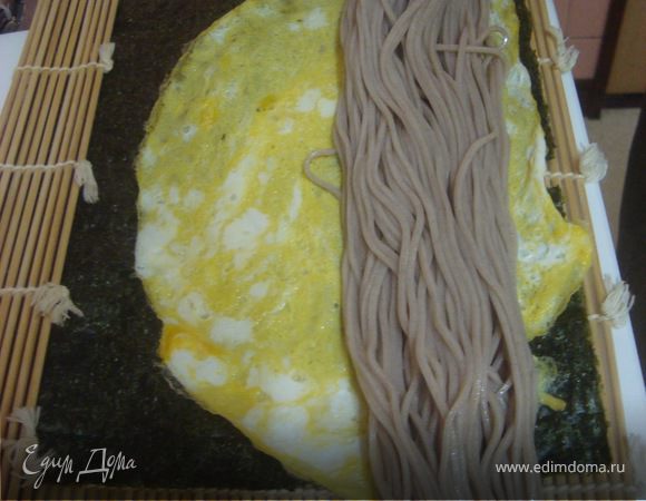 На коврик для приготовления суши кладем подсушенное на огне нори, затем кладем омлет, на него укладываем гречневую лапшу, предварительно хорошо отжатую от воды... Кончик, который мы обвязывали ниткой отрезаем ножом..