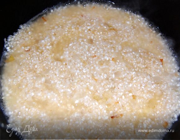 В кастрюле растопить 2/3 сливочного масла, в него всыпать оставшийся лук, обжаривать на медленном огне до прозрачности. Затем всыпать рис и обжарить в масле пару минут. Влить в кастрюлю столько вина, чтобы оно было вровень с рисом, но не покрывало его.