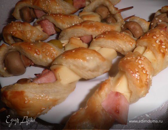 Ветчину и сыр viola нарезать кубиками. 
Берем шпажки и одеваем на них - грибы, ветчину, сыр, оливки. 
Тесто разморозить, раскатать и нарезать на полоски. Обмотать полосками начинку. Готовые шпажки положить на противень. Сверху посыпать кунжутом и тмином. Поставить в горячую духовку на 15-20 минут.Закуска готова!
Приятного аппетита!  

