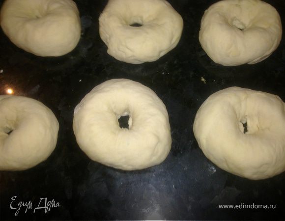 Вскипятить в большой кастрюле воду,подсолить.Духовку нагреть до 200 градусов.Выложить противень бумагой для выпечки.Из теста сформовать 12-15 шариков,сделать в центре отверстие.Колечки теста поочередно спускать в горячую воду на 2 минуты,вынимать.