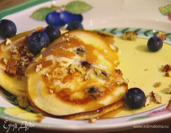 Готовые оладьи полить кленовым сиропом, присыпать орехами и оставшейся голубикой.