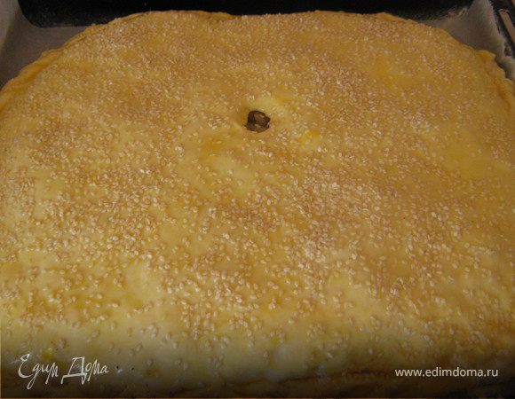 Далее накройте вторым пластом теста, защипните края. В середине сделайте отверстие, смажьте пирог взбитым яйцом, посыпьте кунжутными семечками и поставьте в разогретую до 180°C духовку на 40–45 минут.