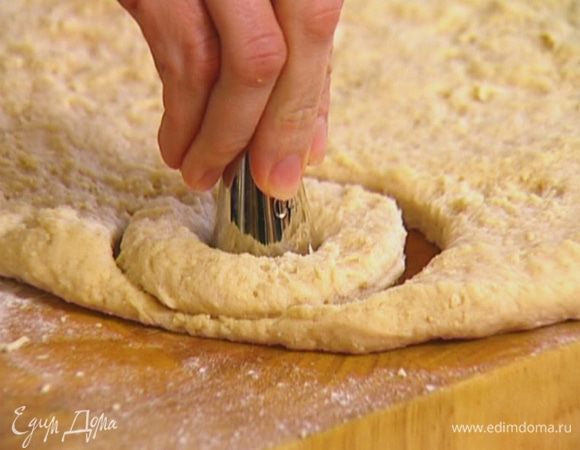 Выложить тесто на рабочую поверхность, сформировать пласт толщиной полтора сантиметра. Кондитерским кольцом сделать из теста кружки, у каждого кружка с помощью формочки меньшего диаметра вырезать середину.