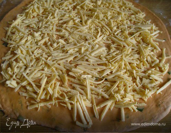 Сыр  натереть  на  терке. Раскатать  тесто  в  пласт  толщиной  1 см. Выложить  сверху  сыр. 