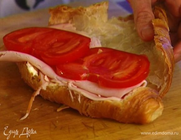 Круассаны разрезать вдоль, не прорезая до конца, затем развернуть, намазать половинку каждого круассана сливочным сыром, выложить сверху ветчину и дольки помидора.