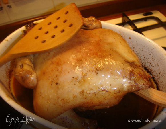 Вставить в брюшко деревянную ложку и придерживая лопаткой верхнюю часть тушки, повернуть курицу спинкой вверх, таким образом, чтобы все чесночное масло и ломтики лимона вылились на дно формы.