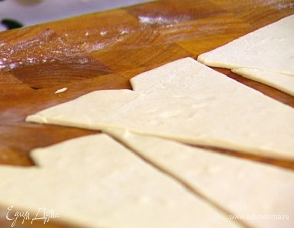 Тесто разморозить, раскатать и нарезать треугольниками — они должны получиться с одним очень острым углом. На стороне, противоположной острому углу, вырезать по центру маленький треугольник.